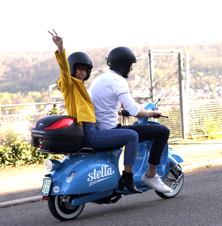 Junge Frau jubelt auf dem Rücksitz einer elektrischen Vespa